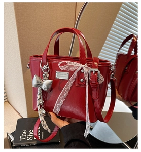Detail of red oil wax leather bucket bag featuring white lace bow and silver metal charm