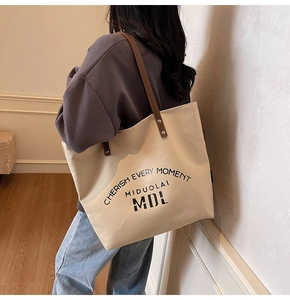 Rear view of a model wearing a large cream canvas tote bag with brown leather straps