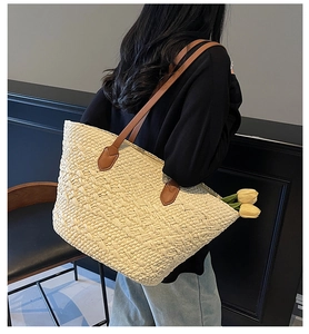 Detail of a large woven straw tote bag featuring brown leather shoulder straps and tulip decor