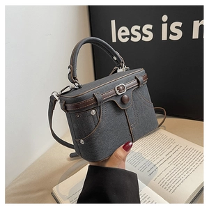 Close-up of retro denim box bag featuring brown leather trim and metal button details