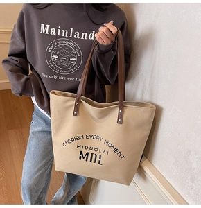 Detail view of canvas tote bag featuring CHERISH EVERY MOMENT print and brown leather straps