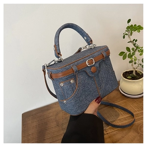 Detail view of denim box bag featuring vintage brown leather trim and metal hardware