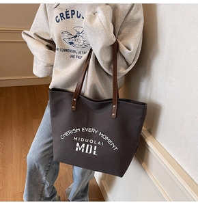 Detail of a large dark grey-brown canvas tote bag with long brown leather straps