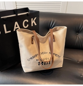 Close-up of beige canvas tote bag with brown leather handles and black slogan print