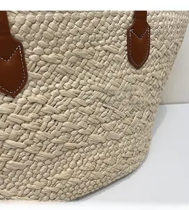Close-up of woven straw tote bag featuring brown leather handles and contrast stitching details
