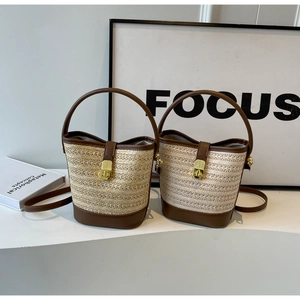 Close-up of woven straw bucket bag with dark brown leather trim and golden twist lock