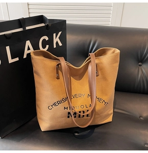 Detail of a khaki canvas tote bag with brown leather straps and black printed text