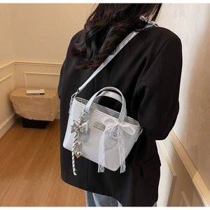 Detail of light blue patent leather bucket bag with silver butterfly charm and lace bow
