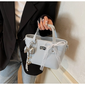 Detail of light blue faux leather handbag featuring lace bow and silver butterfly charm