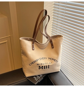 Close-up of beige canvas tote bag with brown leather straps and metal rivet details