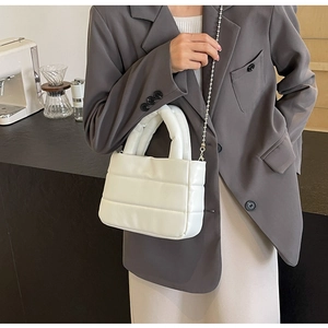 Detailed view of white quilted bucket bag with silver chain strap in cafe setting
