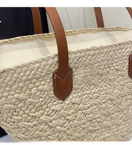 Detail of woven straw tote bag featuring brown leather handles and reinforced stitching