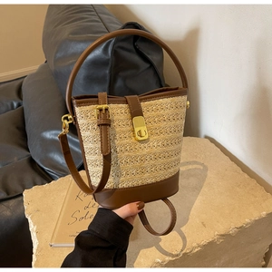Detail of straw bucket bag featuring brown leather trim and golden metal clasp on stone