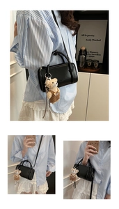 Detail of a black leather Boston bag with teddy bear charm and gold logo lettering