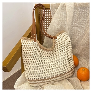 Detail of woven straw tote bag with brown leather handles and rivet accents