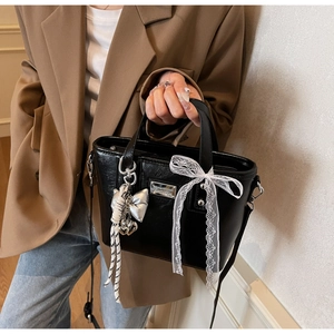 Detail of black oil wax leather bucket bag with lace bow and silver heart pendant charm