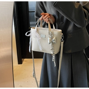 Detail view of cream-white bucket bag with lace bow and silver butterfly charm