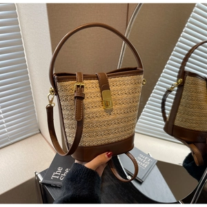 Detail of a straw bucket bag with brown leather trim and gold buckle shown in a mirror