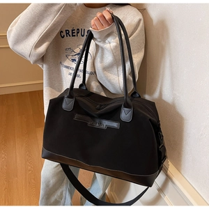 Large black tote bag with leather trim and adjustable shoulder strap held by model