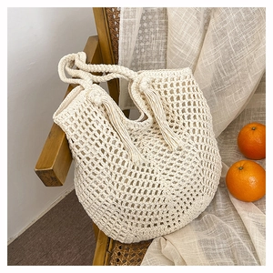 Close-up of beige hand-woven hollow tote bag with intricate tassel details and handle
