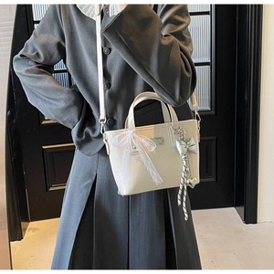 Detail of white faux leather bucket bag featuring lace bow and silver heart pendant