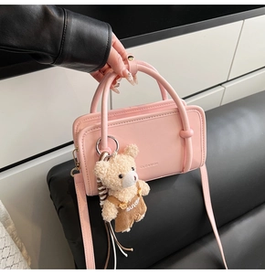 Detailed shot of pink leather handbag featuring embossed logo and cute plush bear charm