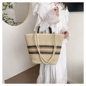 Detail of hand-woven straw tote bag with black stripes and matching handles
