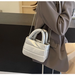 Detailed shot of a silver puffer bucket bag with quilted texture and metal bead chain