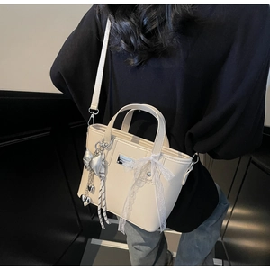 Close-up of cream PU leather tote bag featuring a silver heart bow pendant and lace detail