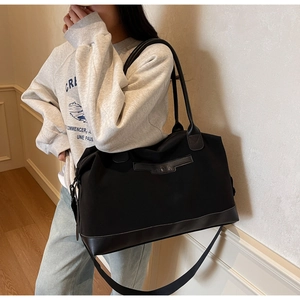 Detail of a large black tote bag with leather base and adjustable metal side buckles