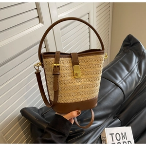 Detailed close-up of woven straw bucket bag with brown leather trim and golden metal buckle