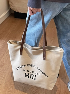 Minimalist off-white canvas tote bag with brown leather handles and black letter print