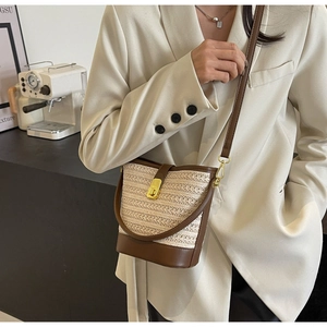 Detail of straw bucket bag with leather trim and gold twist-lock shown with outfit
