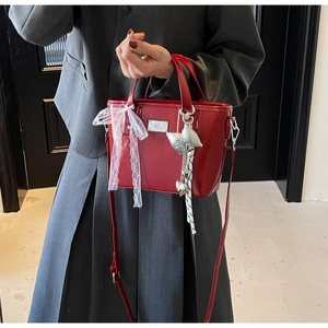 Detail of red oil-wax leather bucket bag featuring lace bow and silver bird charm