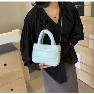 Quilted light blue puffy bucket bag with chain strap held by a model in black shirt
