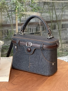 Retro grey denim box handbag with brown leather trim on a wooden outdoor table