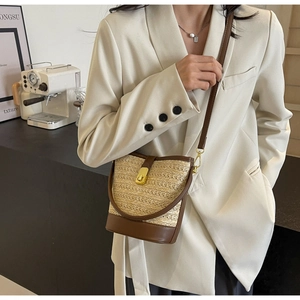 Detail of woven straw bucket bag with dark brown leather trim and gold twist lock