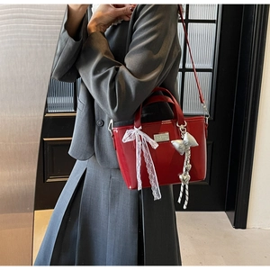 Detail of red oil wax leather handbag featuring white lace bow and silver pendant charms