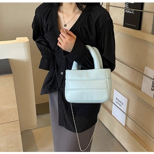 Close-up of light blue quilted bucket bag with silver ball chain and puffy handle detail