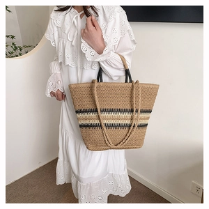 Detail of woven straw tote bag with black stripes and dual straps on white dress model