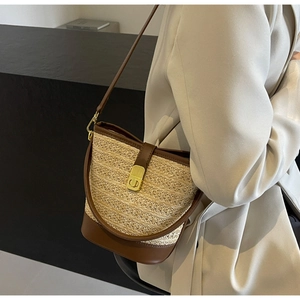 Detail of woven straw bucket bag with brown leather trim and golden twist lock closure