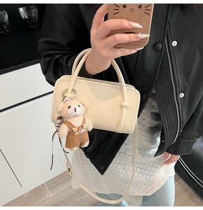 Detail view of cream-colored rectangular handbag with plush bear charm and clear logo