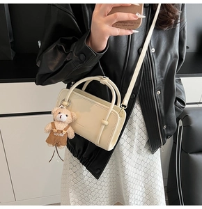 Detail of cream crossbody square bag with a cute brown teddy bear plush charm