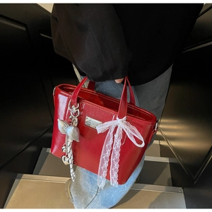 Detail of red glossy oil wax leather bucket bag with silver charm and lace ribbon