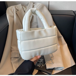 Close-up of white quilted puffer bucket bag featuring thick handle and silver ball chain