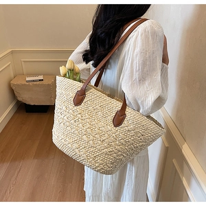 Minimalist beige woven tote bag with brown leather straps shown on a model's shoulder