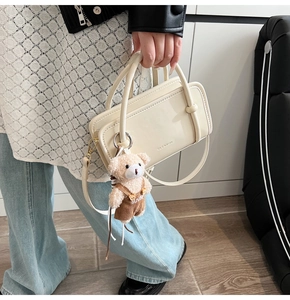 Detail of cream glossy leather handbag featuring a cute teddy bear charm and top handle