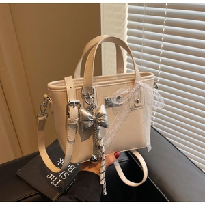 Detail of cream white leather bucket bag with lace ribbons and silver bow charm