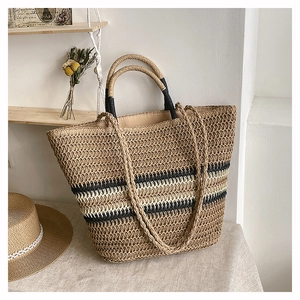 Detail of woven straw tote bag featuring contrast stripes and dual shoulder straps