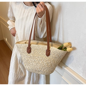 Detail of woven straw tote bag featuring brown leather handles and natural texture